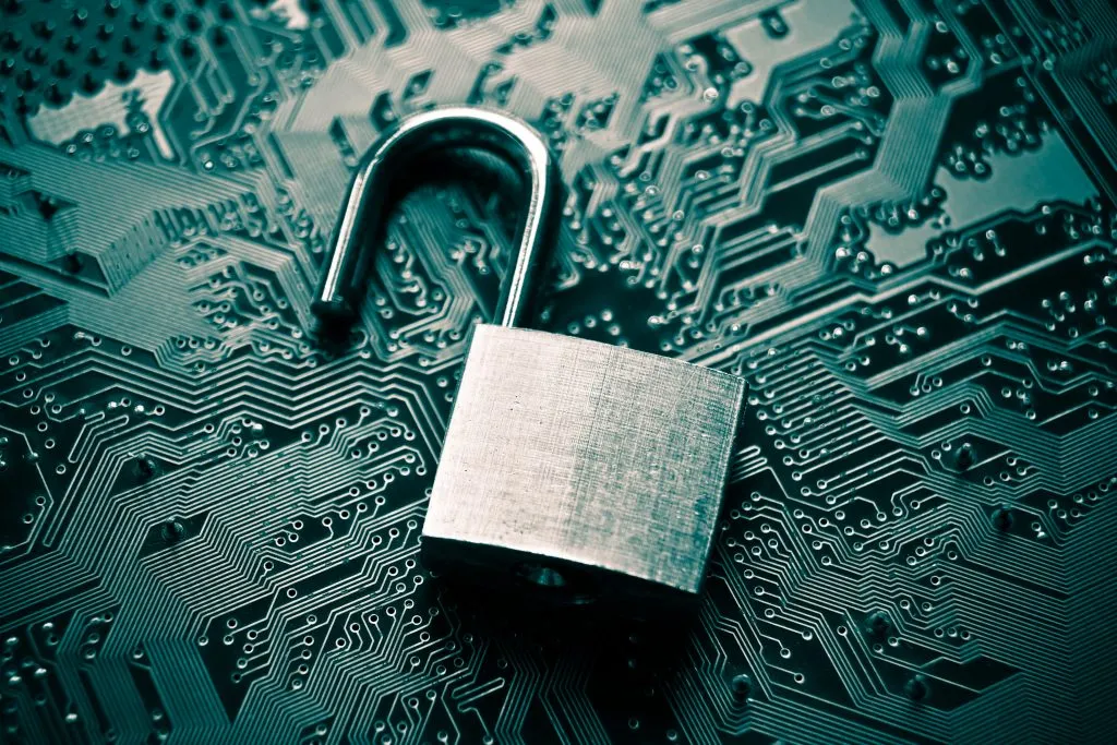 A silver open padlock resting on a dark teal and blue circuit board, symbolizing data security or a breach.